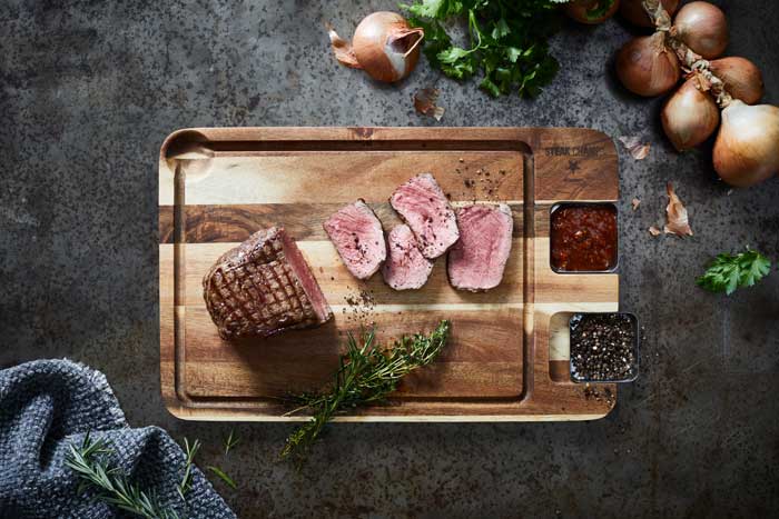 Rózsaszínre sült, szeletelt steak akácia tálalódeszkán, mártásokkal