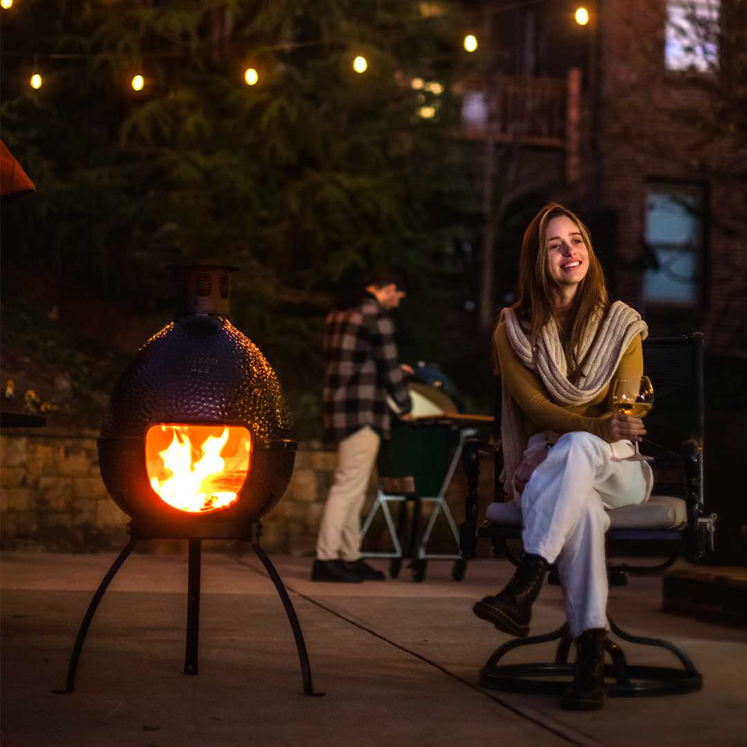 Nő ül a Big Green Egg kerti kandalló mellett borospohárral, hangulatos esti fények között