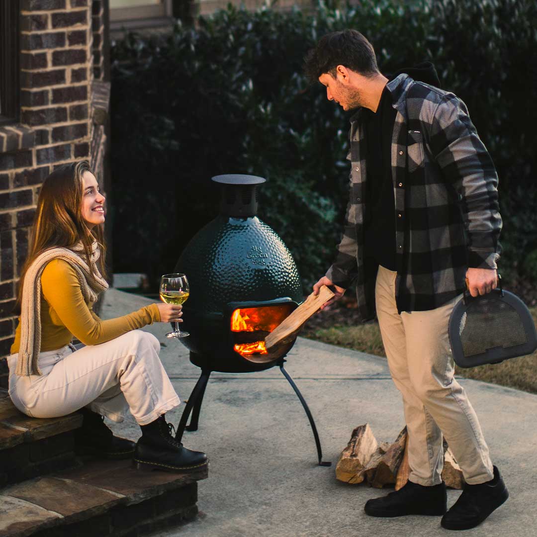 Férfi fa hasábokat helyez a Big Green Egg Chiminea kandallóba, kültéri használat közben