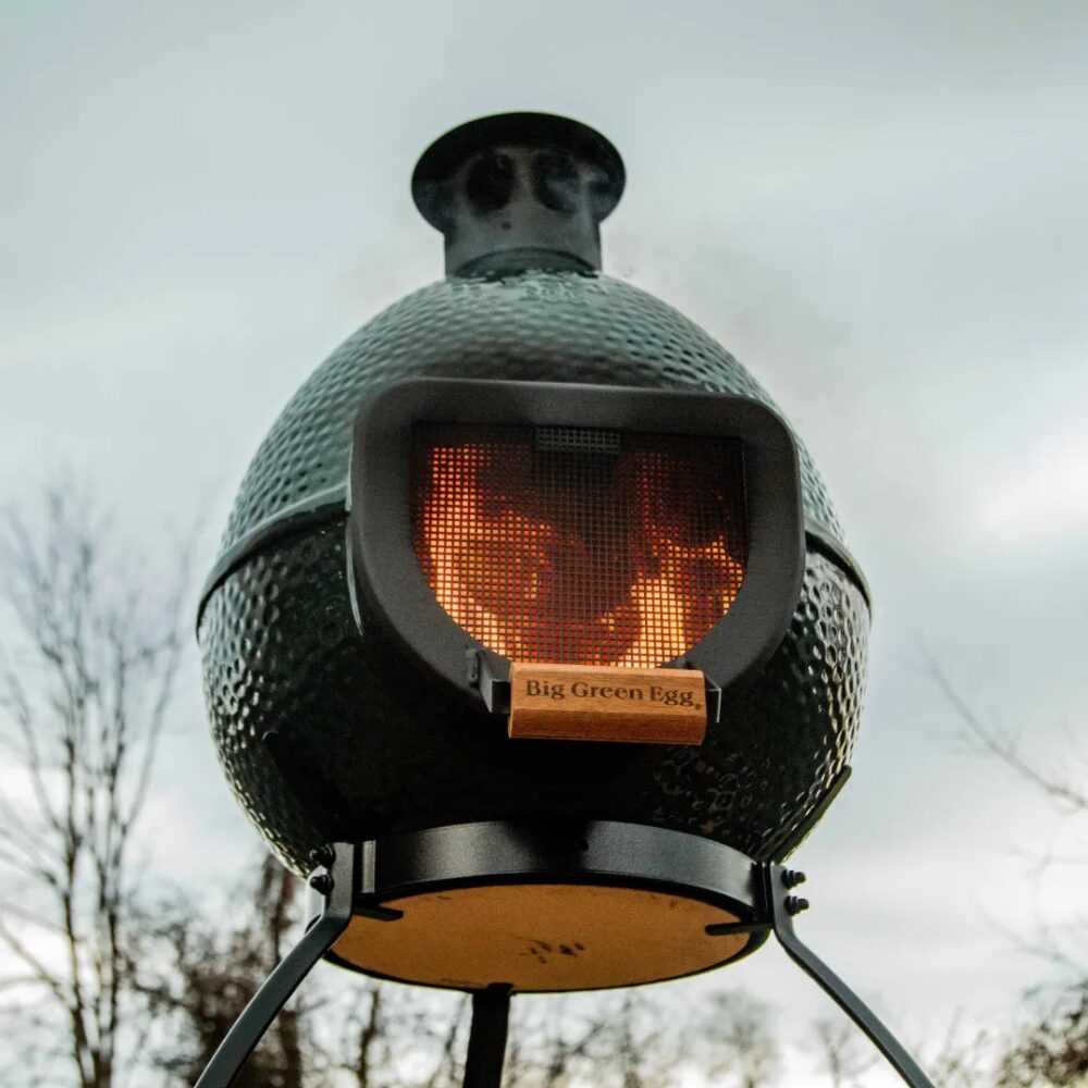 Égő kandalló közelről fotózva, acélrács mögött lobogó tűzzel, Big Green Egg logóval