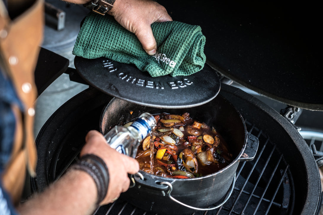 Öntöttvas Big Green Egg lábasban készült étel grillezés közben, zöldségekkel és szósszal.