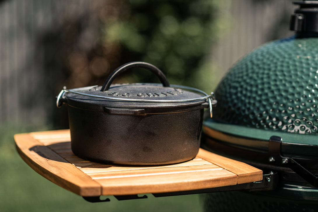 Big Green Egg öntöttvas lábas fa oldaltárolón, kültéri grillező mellett elhelyezve.