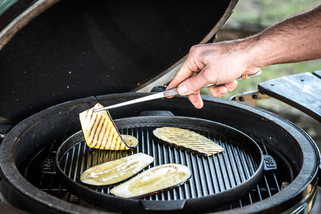 Grillezett padlizsánszeletek készülnek öntöttvas planchán Big Green Egg kerámia grillben, kézi grillcsipesszel forgatva.
