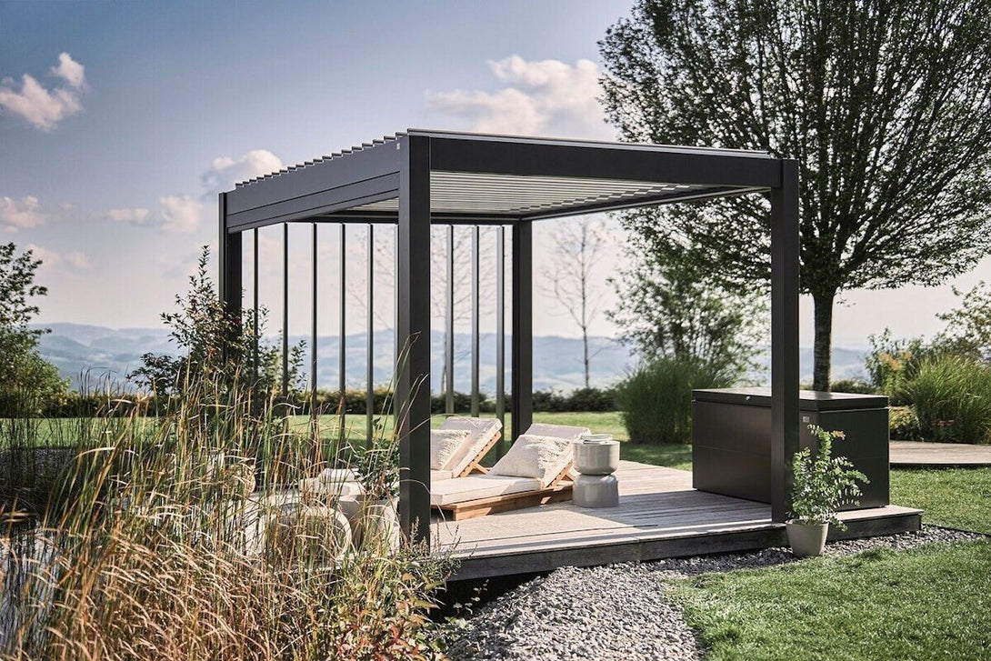 Biohort pergola sötétszürke-metál színben, modern napozóteraszra helyezve, fa napozóágyakkal és tárolóval, festői természeti környezetben.