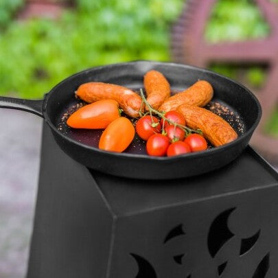 Cook King 28 cm öntöttvas serpenyő grillezett kolbásszal és paradicsommal kültéri használat közben