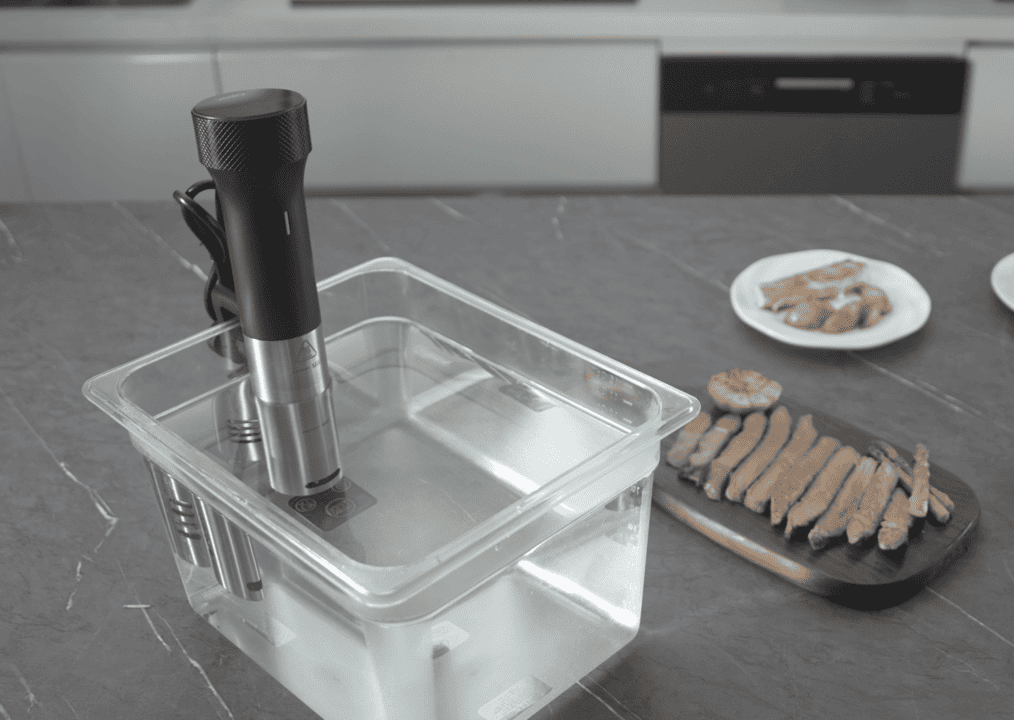 SV80s sous-vide rúd polikarbonát medencében működés közben, felszeletelt húsok a háttérben.